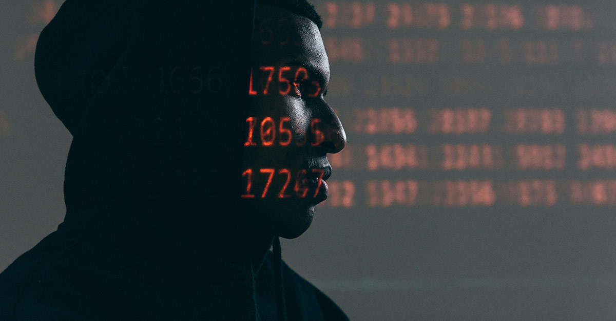 Man in dark hood with red code projected on his face